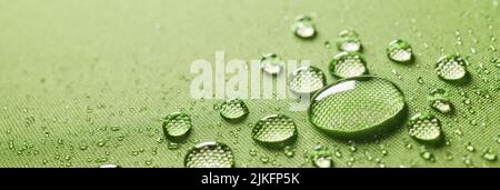 Background closeup of small round transparent clean drops on wet protective green waterproof impregnated textile with various small water drops Stock Photo