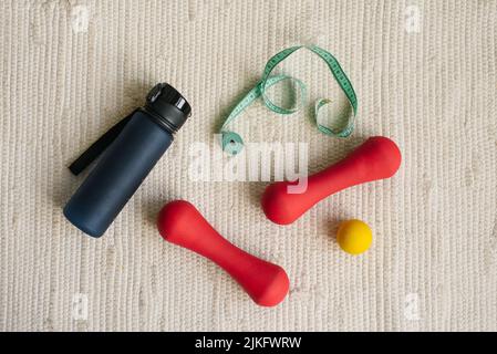 Flat lay of red dumbbell, centimeter, sports equipment, fitness items, water bottle, top view Stock Photo