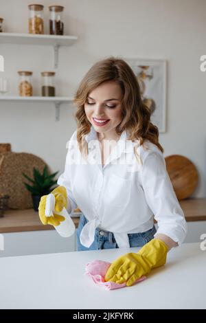 Housewife in yellow gloves wipes the kitchen table Stock Photo