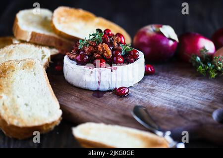 Baked Camembert Brie cheese with a cranberry, honey, balsamic vinegar and nut relish and garnished with thyme. Served with toasted bread slices. Stock Photo