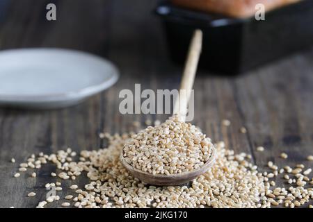 Wooden spoon filled with hard white wheat berries. Selective focus with blurred foreground and background. Loaf of bread in background. Stock Photo