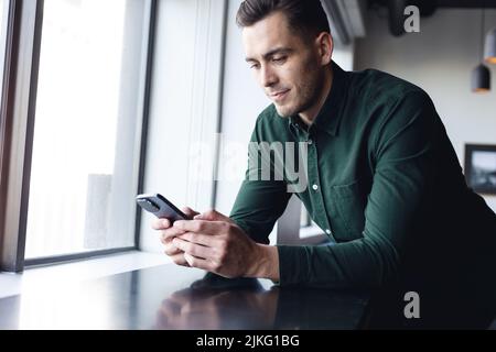Caucasian young businessman text messaging through mobile phone in creative office Stock Photo