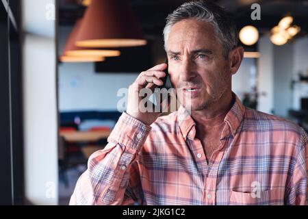 Caucasian mature businessman talking on smart phone in creative office Stock Photo