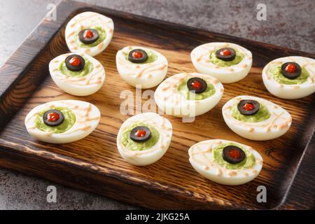 Delicious deviled eggs stuffed with guacamole and olives close-up on a wooden tray on the table. horizontal Stock Photo