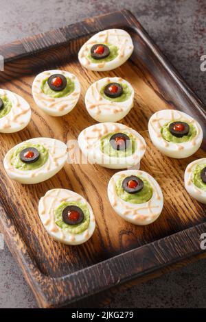 Guacamoldy Eyeballs Eggs stuffed with avocado cream in a wooden tray on the table. Vertical Stock Photo