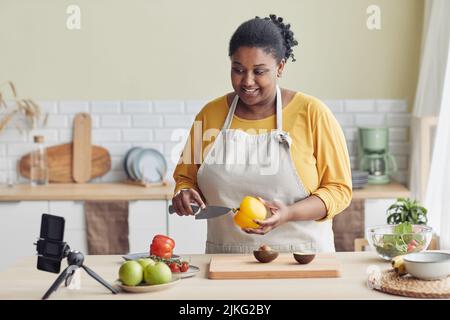 Portrait of young black woman cooking healthy meal in kitchen and recording video, copy space Stock Photo