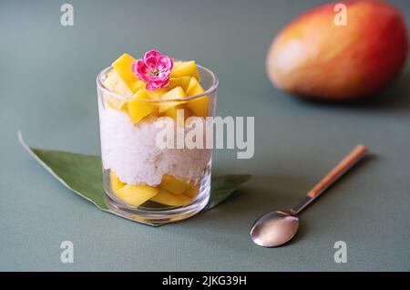 Thai dessert with mango and sticky rice and coconut milk decorated by carnation, sugarcane leaf, raw mango backside Stock Photo