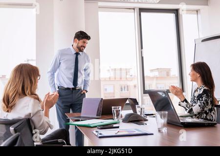 Group of business people clapping hands after a meeting in board room. Businesswomen sitting at desk while businessman presenting his financial plan. Stock Photo