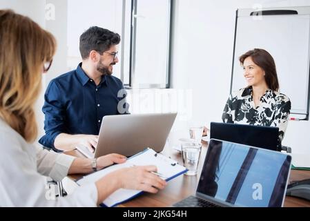 Businesswomen and businessman sitting at desk and using laptop while having a meeting in a conference room. Stock Photo