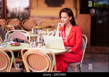 Attractive woman looking thoughtfully and using a laptop while sitting at outdoor cafe terrace. Stock Photo