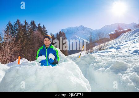 Boy in ski winter outfit prepare snowballs inside snow fortress Stock Photo