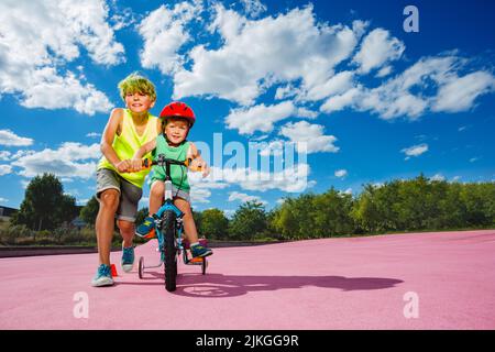 Portrait big boy push little bicycle teach to ride a bike Stock Photo