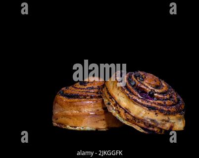 Image of two buns with poppy seeds, cinnamon and cherries on a black background Stock Photo