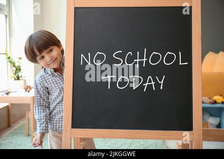 Cute little boy and chalkboard with written text NO SCHOOL TODAY in classroom Stock Photo