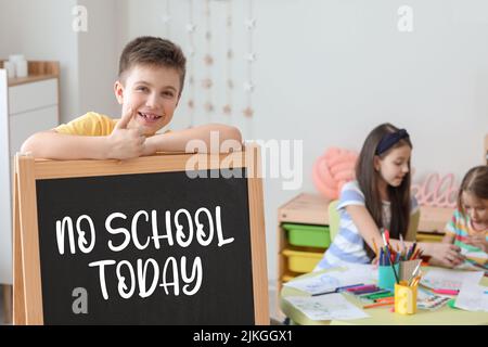 Happy little boy and chalkboard with written text NO SCHOOL TODAY in classroom Stock Photo