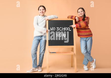 Cute twin girls and blackboard with text NO SCHOOL TODAY on color background Stock Photo