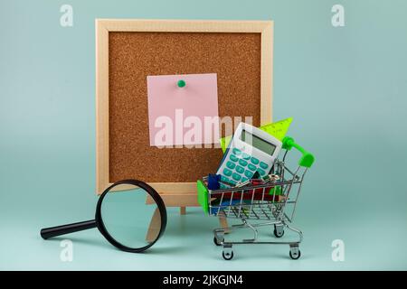 Cork board with note, magnifier and stationery in a shopping cart. Shopping for school. Stock Photo
