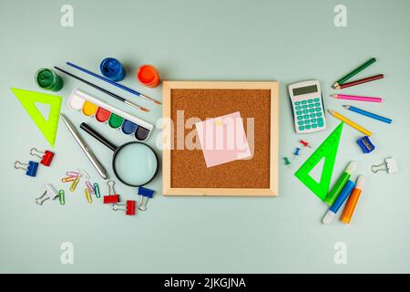 Back to school concept. Cork board near colorful school or office supplies on green table. Flat lay, top view, copy space. Stock Photo