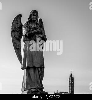 Low-angle shot of sculpture of an angel woman against the background of church tower, black and white background.Tourist attraction Stock Photo