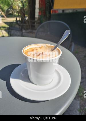 A vertical closeup of a cup of cappuccino on a table of a cafe in sunlight Stock Photo