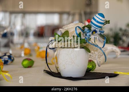 A beautiful shot of a decorative Easter egg in a ceramic vase with a white rose on a table Stock Photo