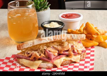 A sandwich with ham and sauerkraut on checkered napkin next to fried potato, sauces, and orange juice Stock Photo