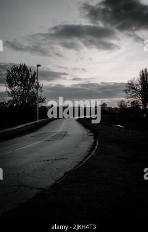 A vertical black and white shot of a road in a rural area in cloudy sky background Stock Photo