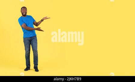 Excited Black Guy Gesturing Pointing At Free Space, Yellow Background Stock Photo