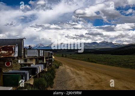 A line of mailboxes with a road and mountain range in the background Stock Photo
