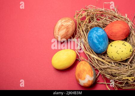 A beautiful view of colored eggs three of them in a nest and three next to it isolated on a pink background Stock Photo