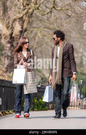 London shoppers; walking home. A young mixed race couple discuss their plans after a day out shopping. From a series of images. Stock Photo