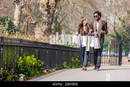 London shoppers; togetherness. A young mixed race couple walking home with their bags after a day out shopping. From a series of images. Stock Photo