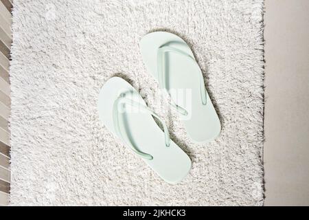 Pair peppermint-coloured flip-flops on white carpet in bathroom. Concept of cleanliness and personal care, top view Stock Photo