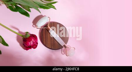 Top view of facial roller for massage on wooden slice.Pastel pink color,eco friendly concept. Stock Photo