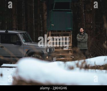 The driver in jacket standing next to his gray Suzuki Jimny car in winter Stock Photo