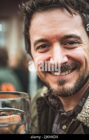 A vertical shot of a Caucasian bearded man smiling in close up while holding a beer Stock Photo