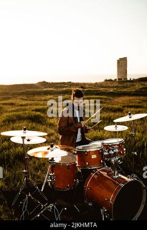 A vertical shot of a young man playing drums in a green field Stock Photo