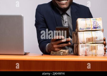 african businessman using his phone next to a lot of money Stock Photo