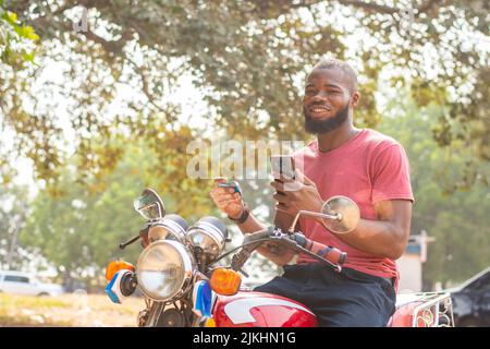 african man on a bike using phone and credit card Stock Photo
