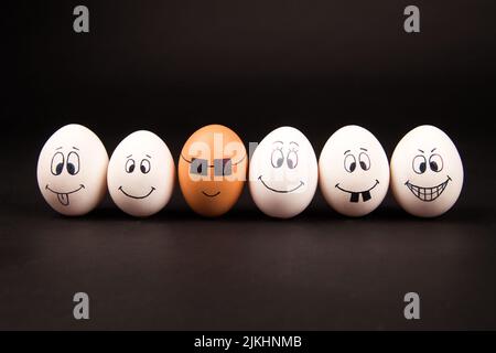 A closeup of funny and silly faces on white and brown eggs on a black surface Stock Photo