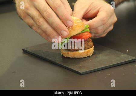 A closeup shot of the chef's hands putting a bun on a mini burger Stock Photo