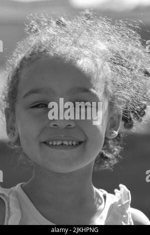 a vertical shot of small girl smiling in grayscale Stock Photo