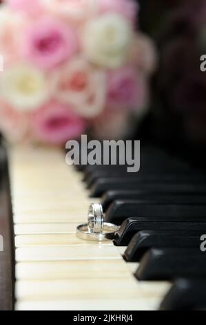 A vertical shot of the wedding rings on the piano keys with the bouquet in the background Stock Photo