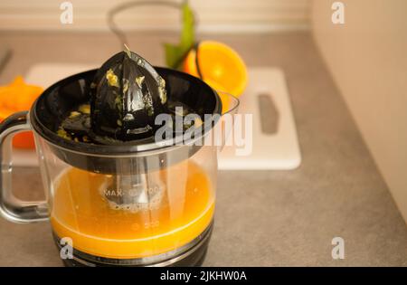man squeezing fresh orange fruit on a juicer. Preparing healthy breakfast from natural ingredient. Organic vitamin drink Stock Photo