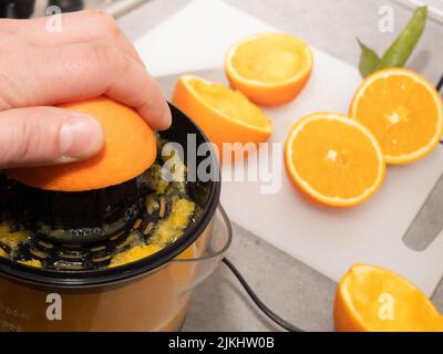 man squeezing fresh orange fruit on a juicer. Preparing healthy breakfast from natural ingredient. Organic vitamin drink Stock Photo