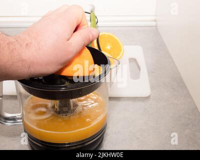 man squeezing fresh orange fruit on a juicer. Preparing healthy breakfast from natural ingredient. Organic vitamin drink Stock Photo