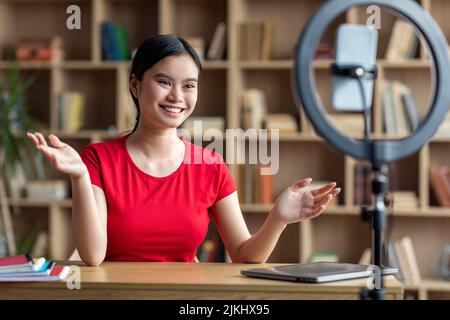 Inspired pretty smiling teen japanese lady shooting blog for student on smartphone in office interior