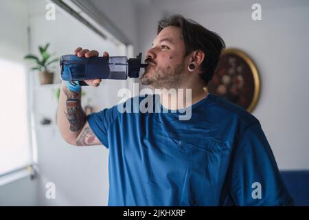 A Caucasian male with a blue t-shirt drinking from a Water Bottle  practicing sports at home Stock Photo