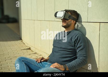 Smiling man using virtual reality (VR) glasses outdoors on a sunny day Stock Photo
