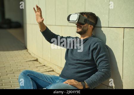 Smiling man using virtual reality (VR) glasses outdoors on a sunny day Stock Photo